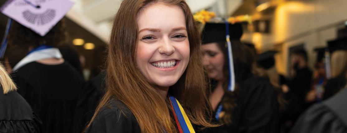 毕业后，一名学生站在人群中，对着镜头微笑